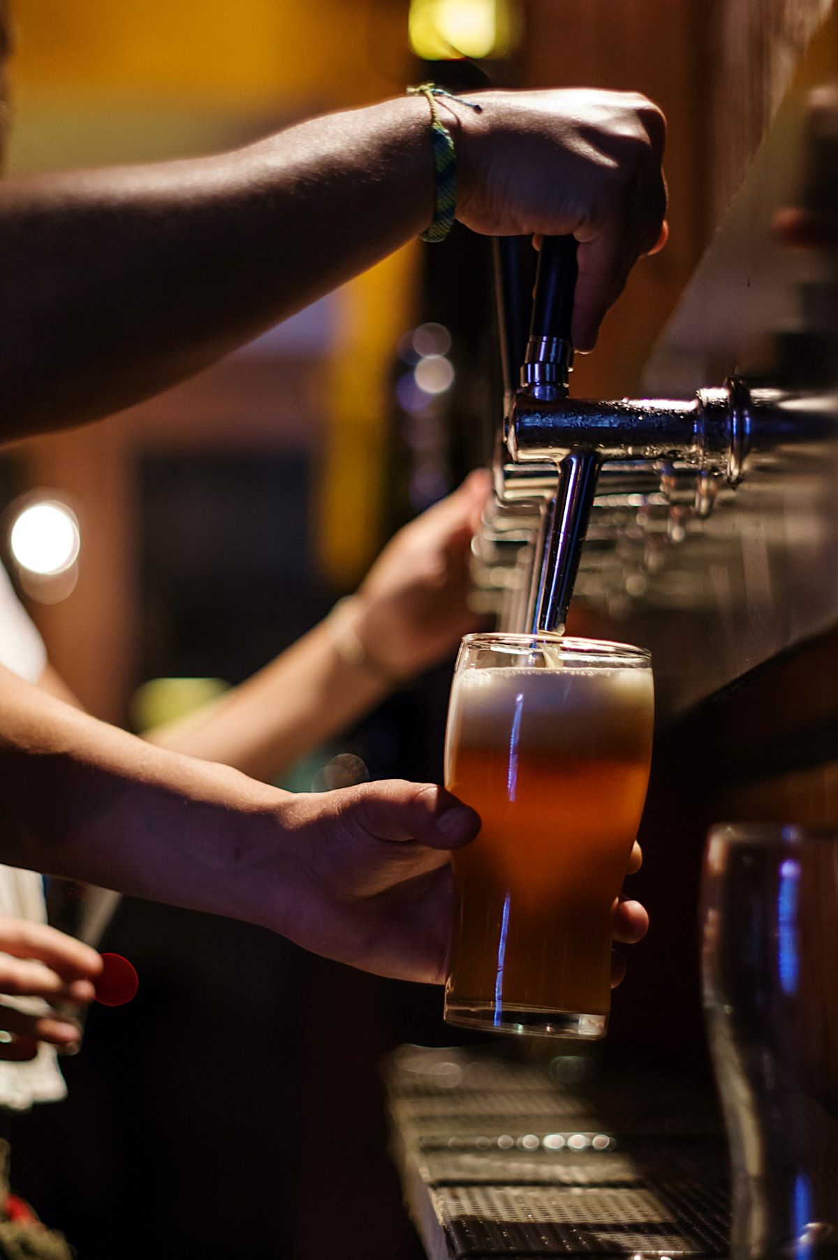 A bartender pouring a draft beer for people. 