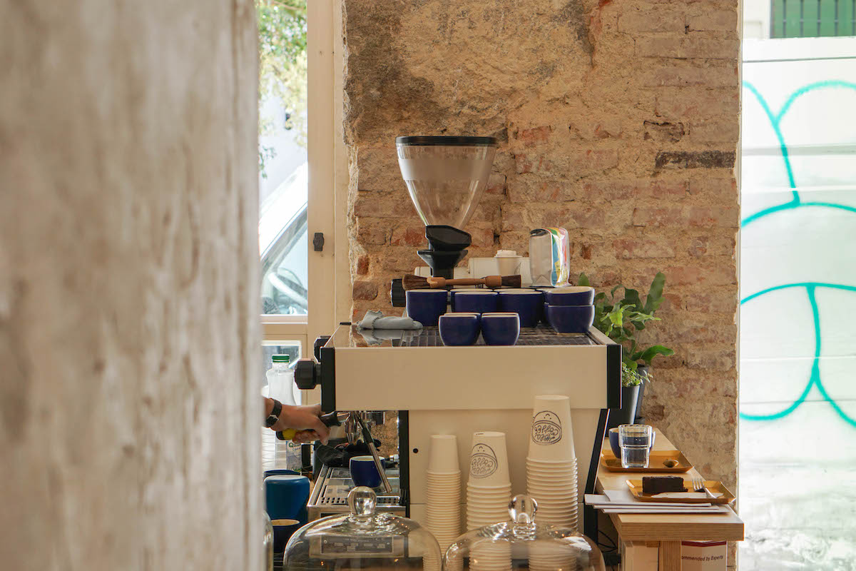 Counter at a coffee shop with an espresso machine, white paper cups, and blue mugs.