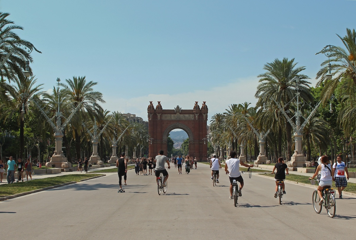 people riding bikes in barcelona down a street with palm trees