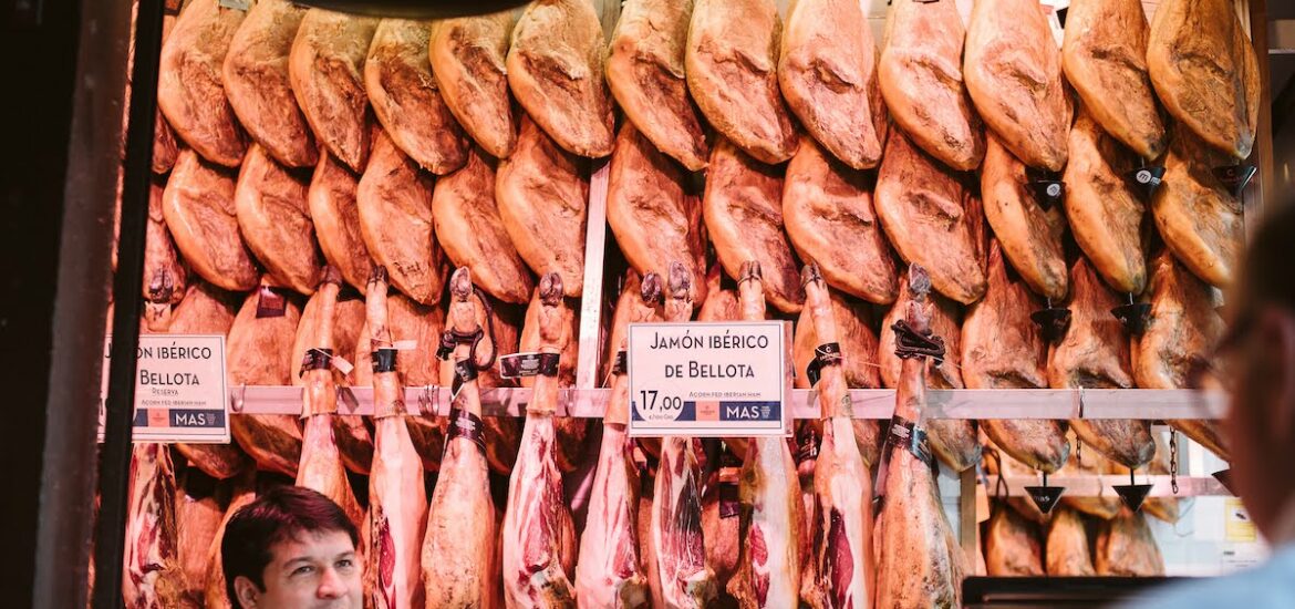 Several legs of cured Iberian ham hanging on the wall at a food market.