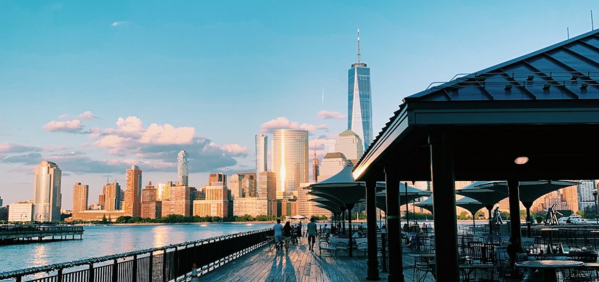 View looking down a riverside promenade towards the Manhattan skyline