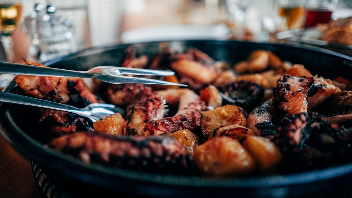 Tongs pulling a grilled octopus leg out of a cast iron skillet