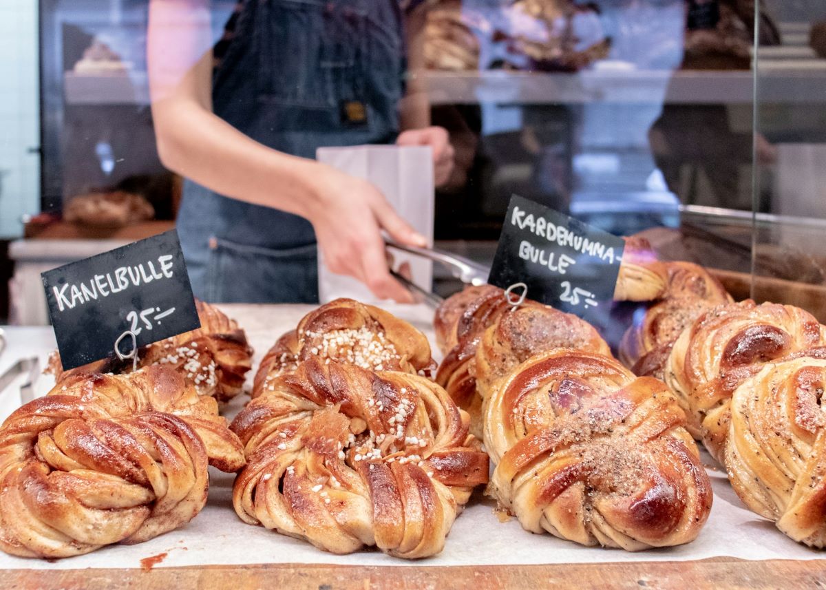 A bakery worker selecting a kanelbulla from a pastry case. 