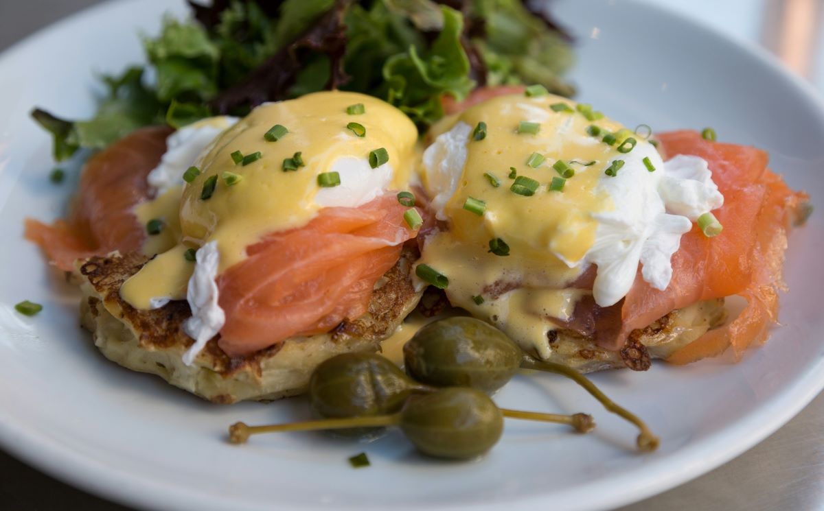 A ceramic plat with eggs benedict and creamy hollandaise sauce. 