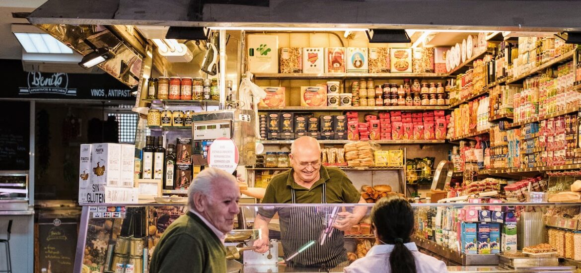 Vendor at a market stall smiling while serving customers.