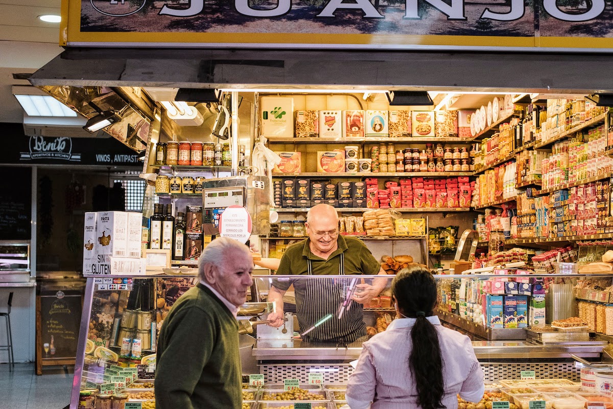 Vendor at a market stall smiling while serving customers.