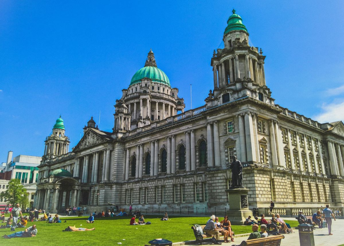 People sitting in the grass outside of Belfast City Hall on a warm spring day.