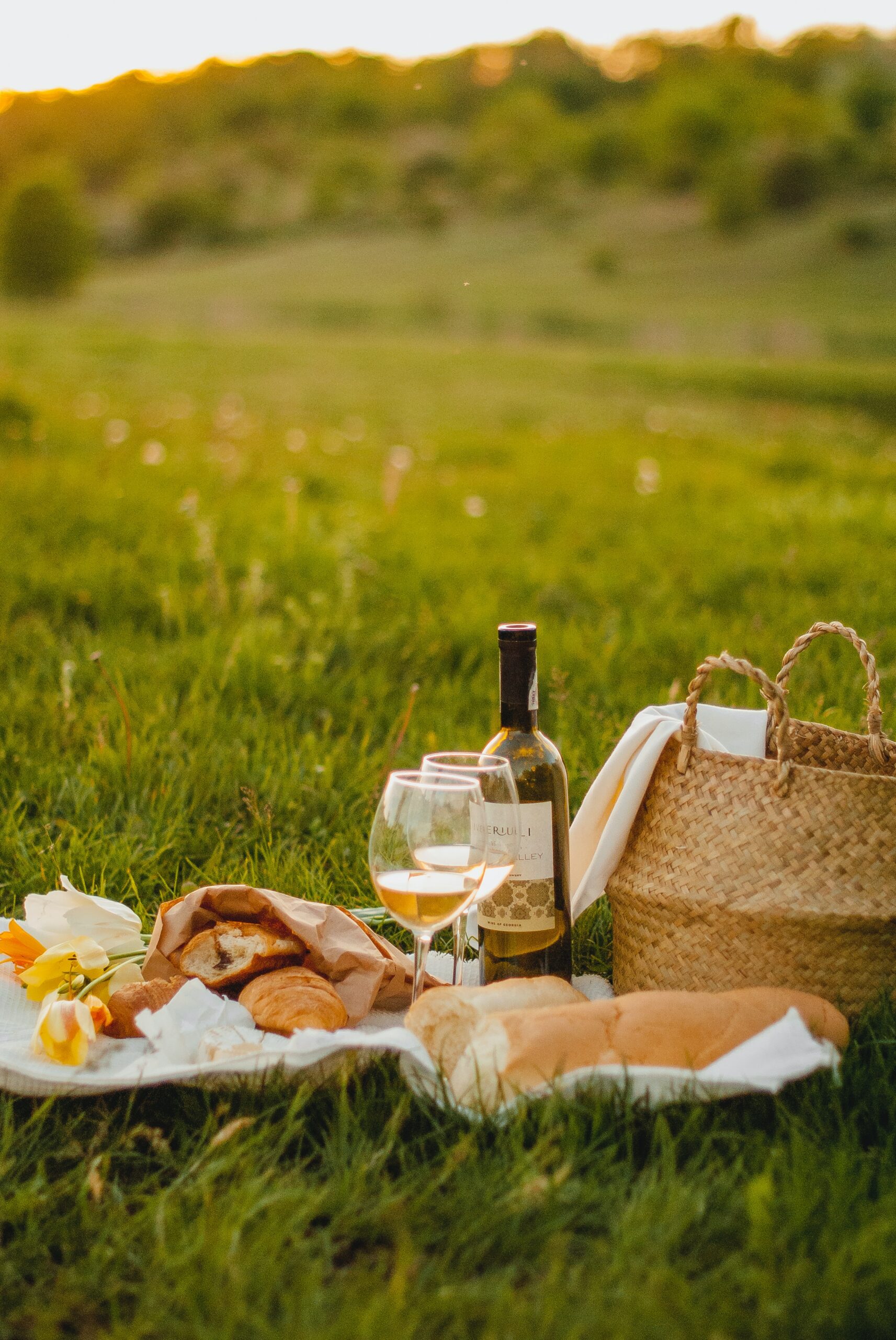 A bottle of wine and some bread sitting on the grass at a picnic