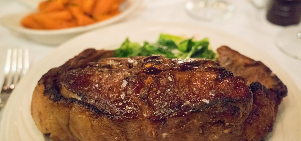 Piece of steak sprinkled with coarse salt on a white plate with a serving of greens in the background