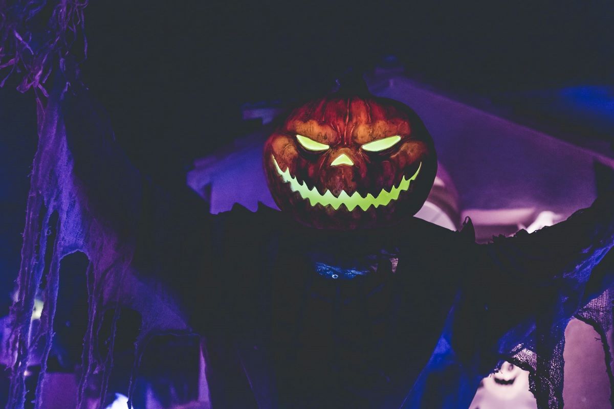 A person wearing a jack o lantern in front of a haunted house. 