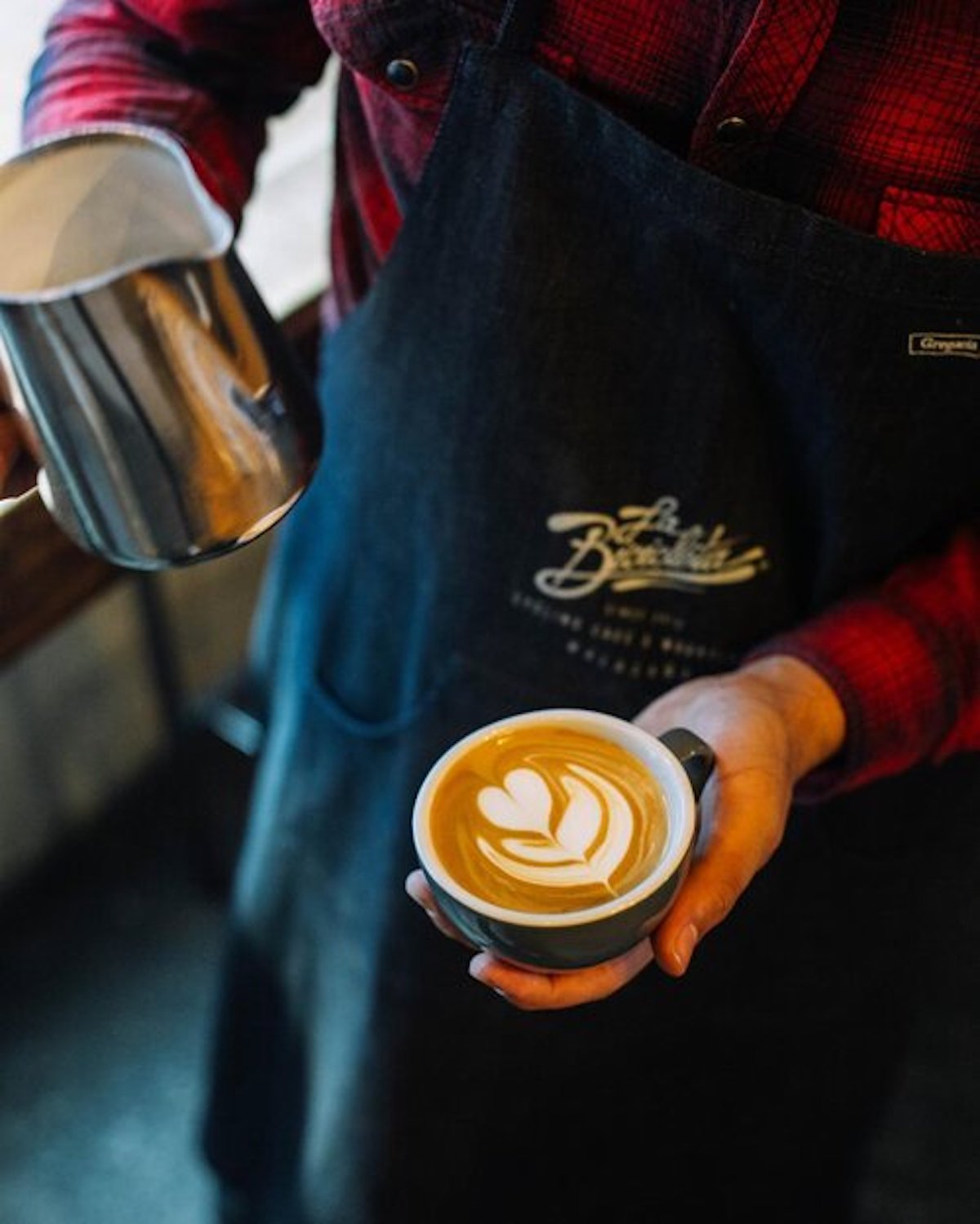 Barista holding a silver pitcher of milk and a latte
