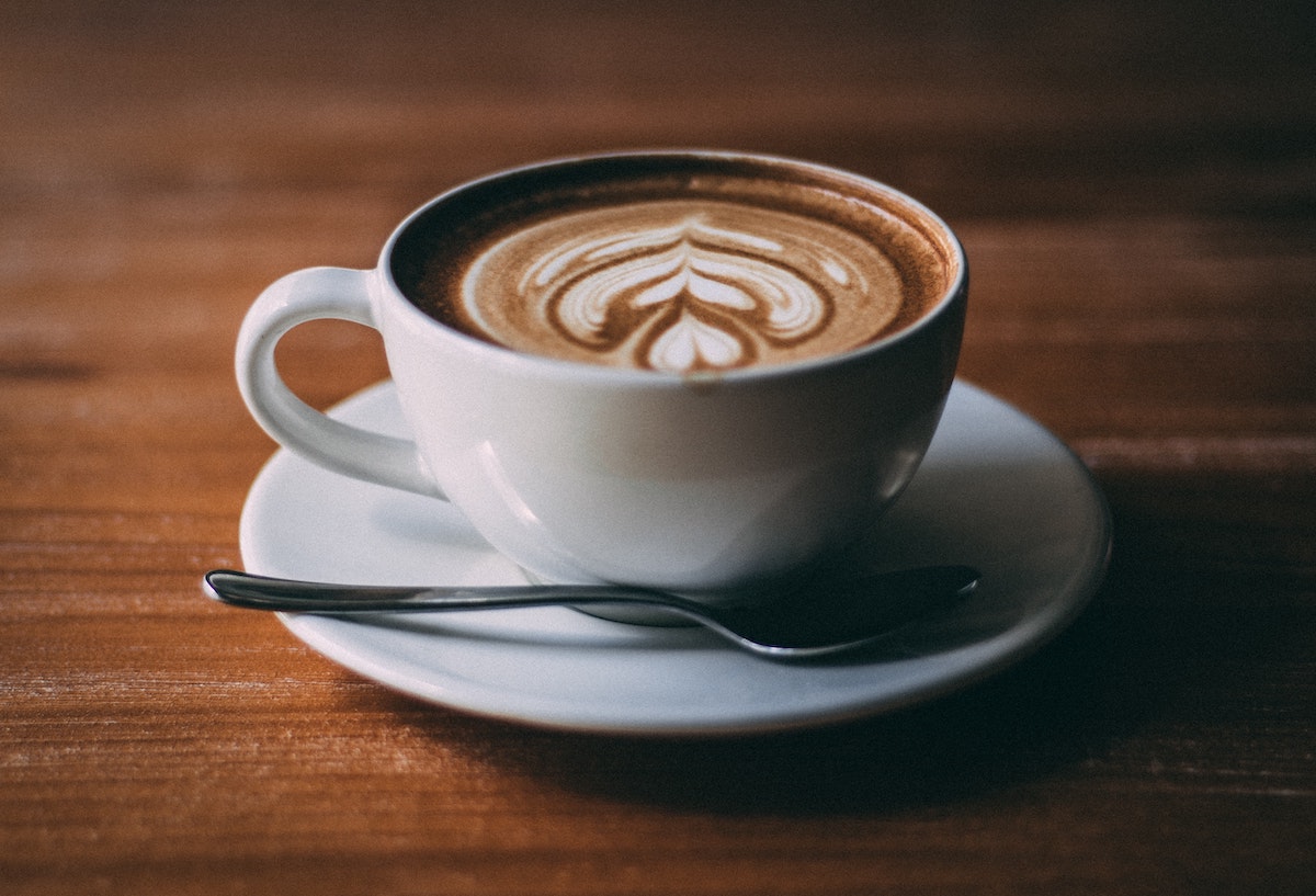 Latte in a small white mug atop a wooden table