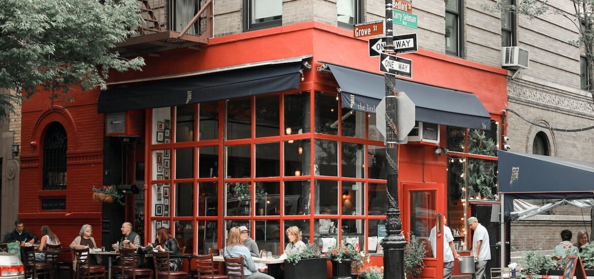 Exterior of a restaurant on a city street corner with red paneling around the windows and black awnings