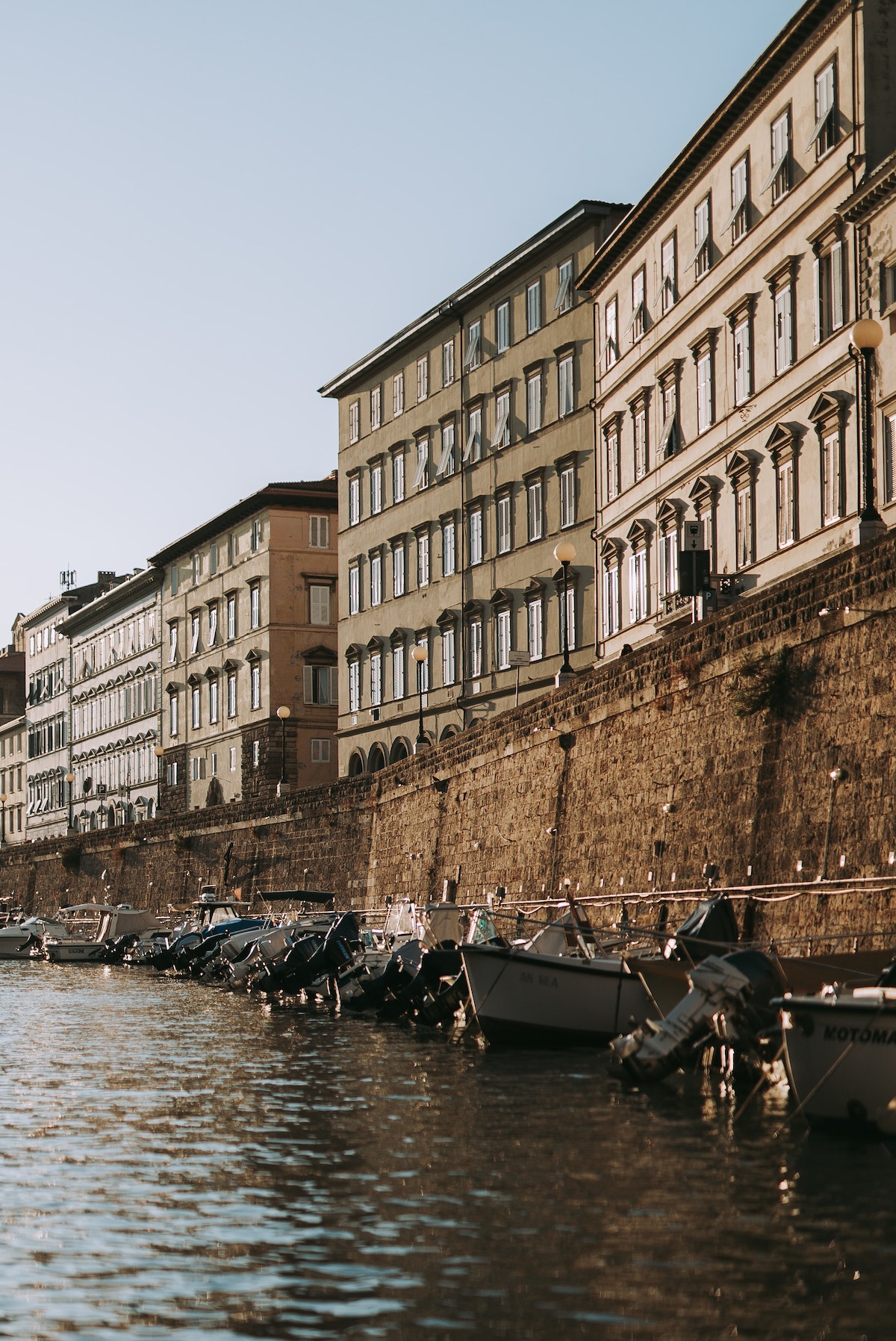 Multi-story stone buildings along a waterfront with small fishing boats along the edge