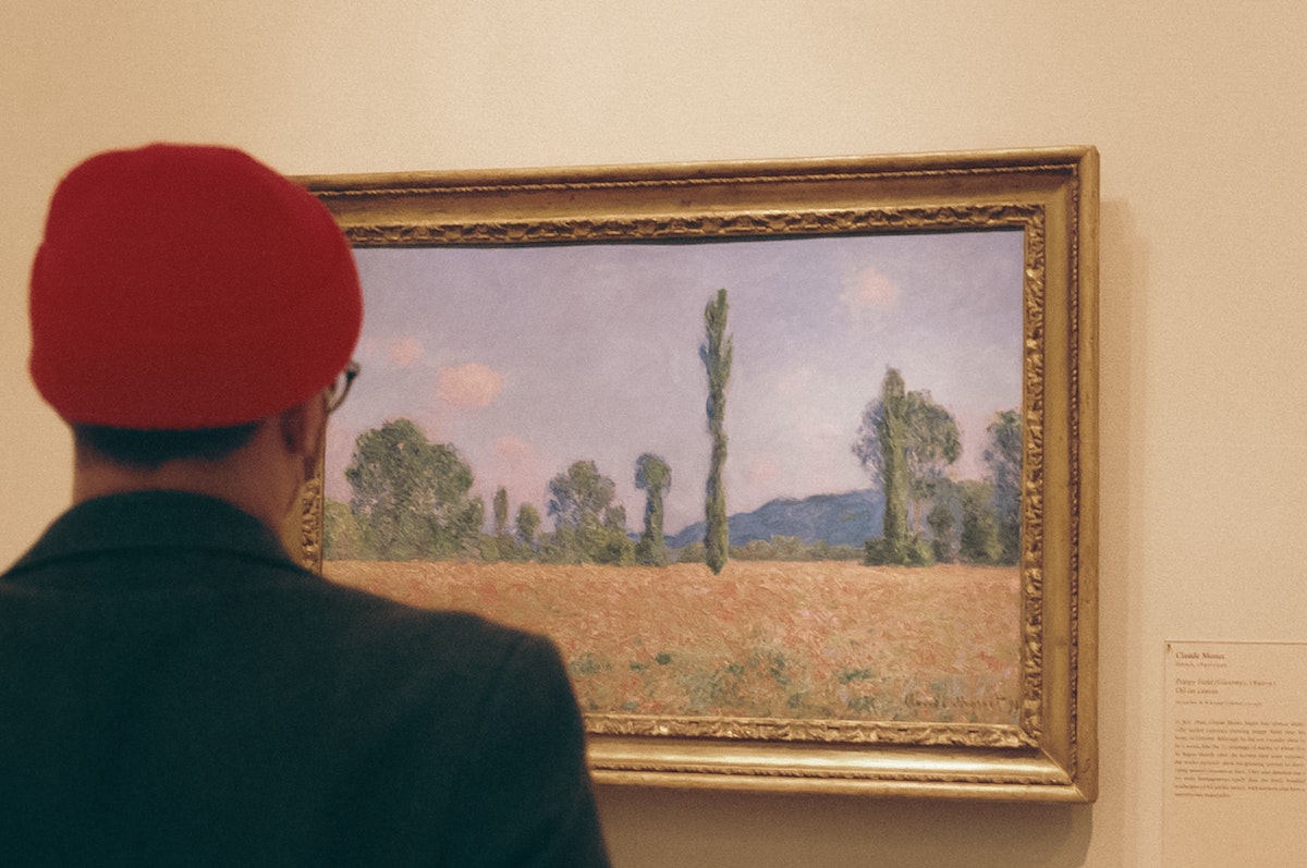 A person wearing a red hat is looking at a landscape painting by Monet