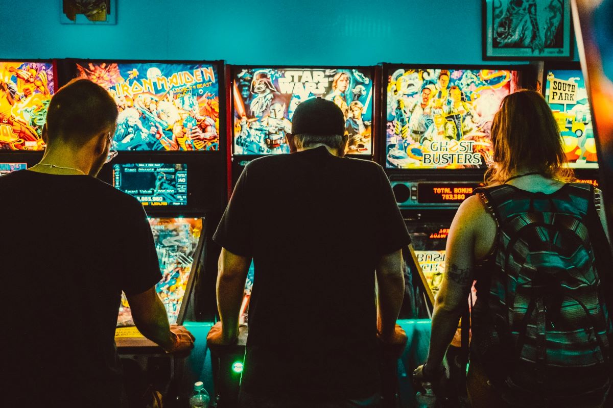 three people playing pinball at a bar in Bordeaux.