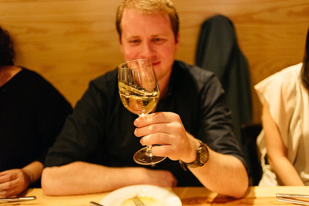 Man seated at a table swirling a glass of white wine.