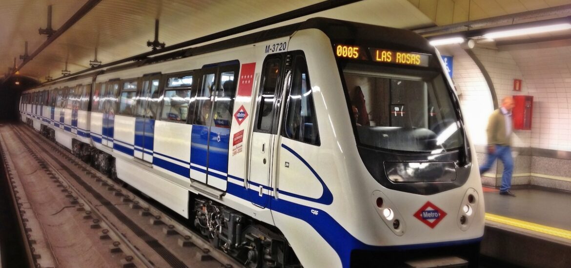 A white and blue train of the Madrid metro arriving at a station.