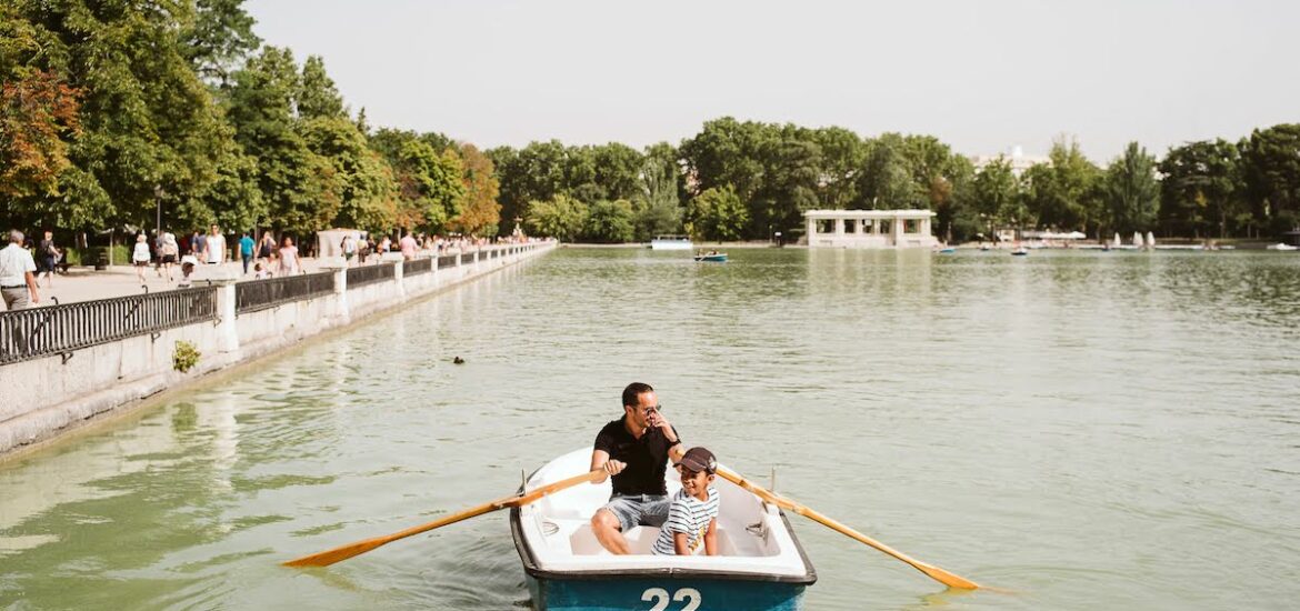 A father with his young son rowing a boat around a small lake.