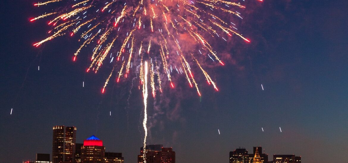 A huge red and white firework explodes over the Boston skyline on the Fourth of July, one of the most fun Festivals in Boston