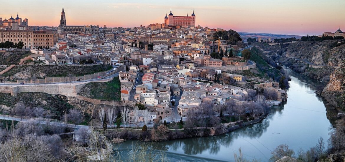 Panoramic view of Toledo, Spain at sunset taken from across a river.