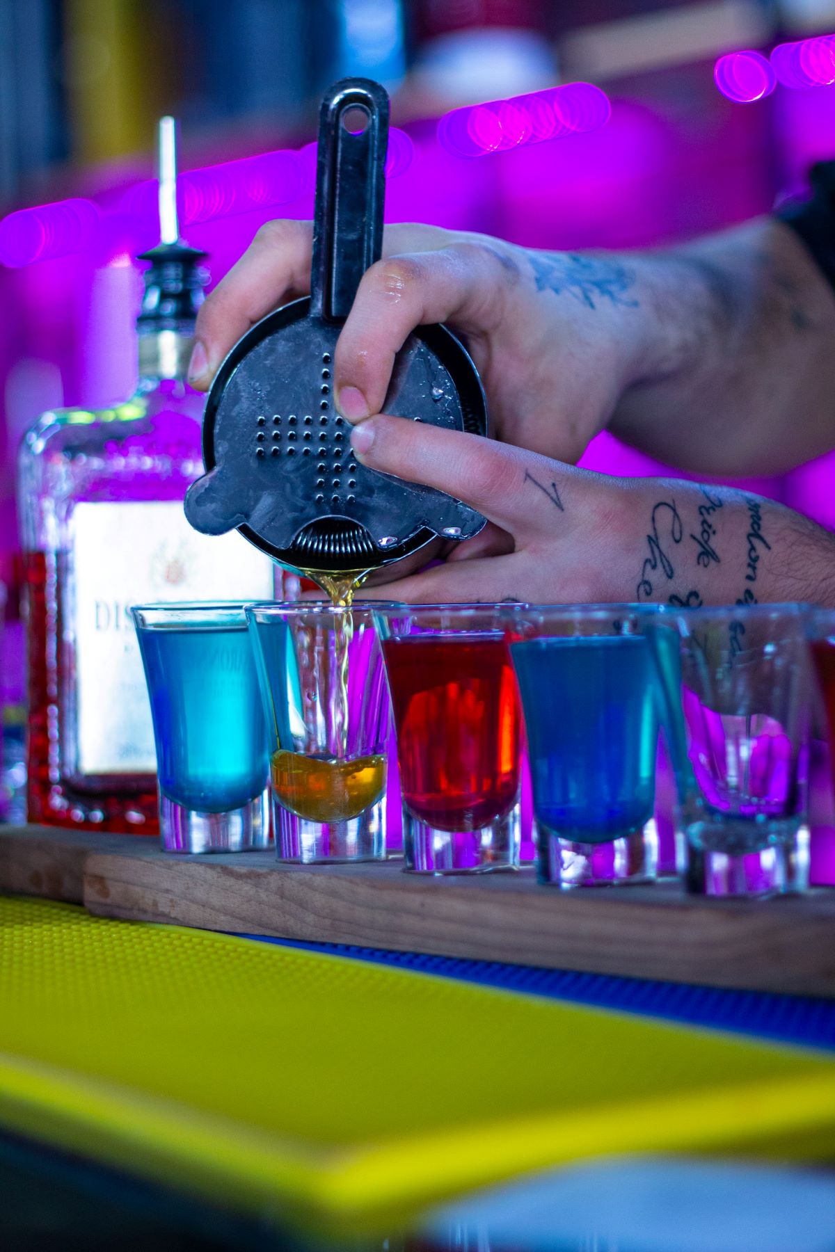 A bartender preparing a bunch of different colored shots. 