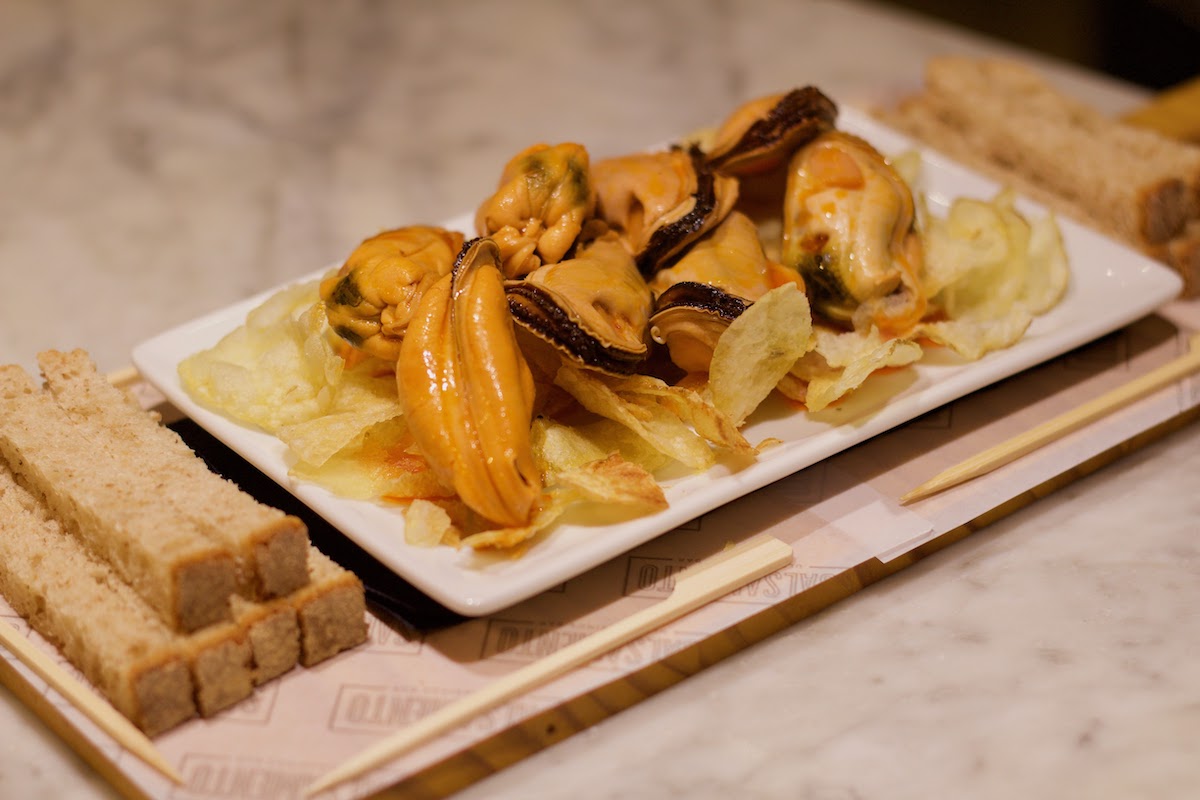 Canned mussels served over potato chips on a wooden board