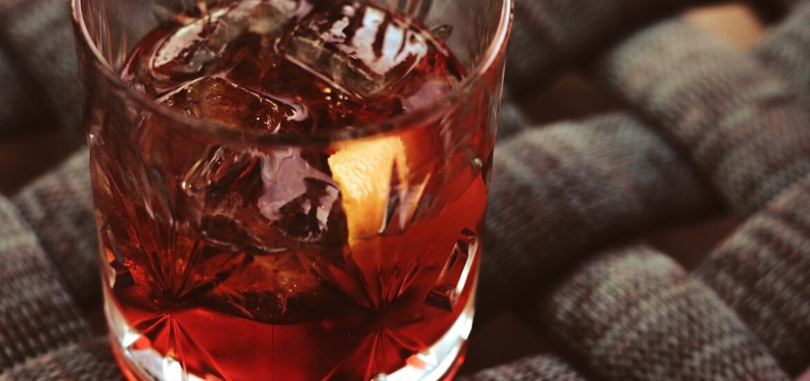 Brown cocktail in a short glass atop a woven black surface.