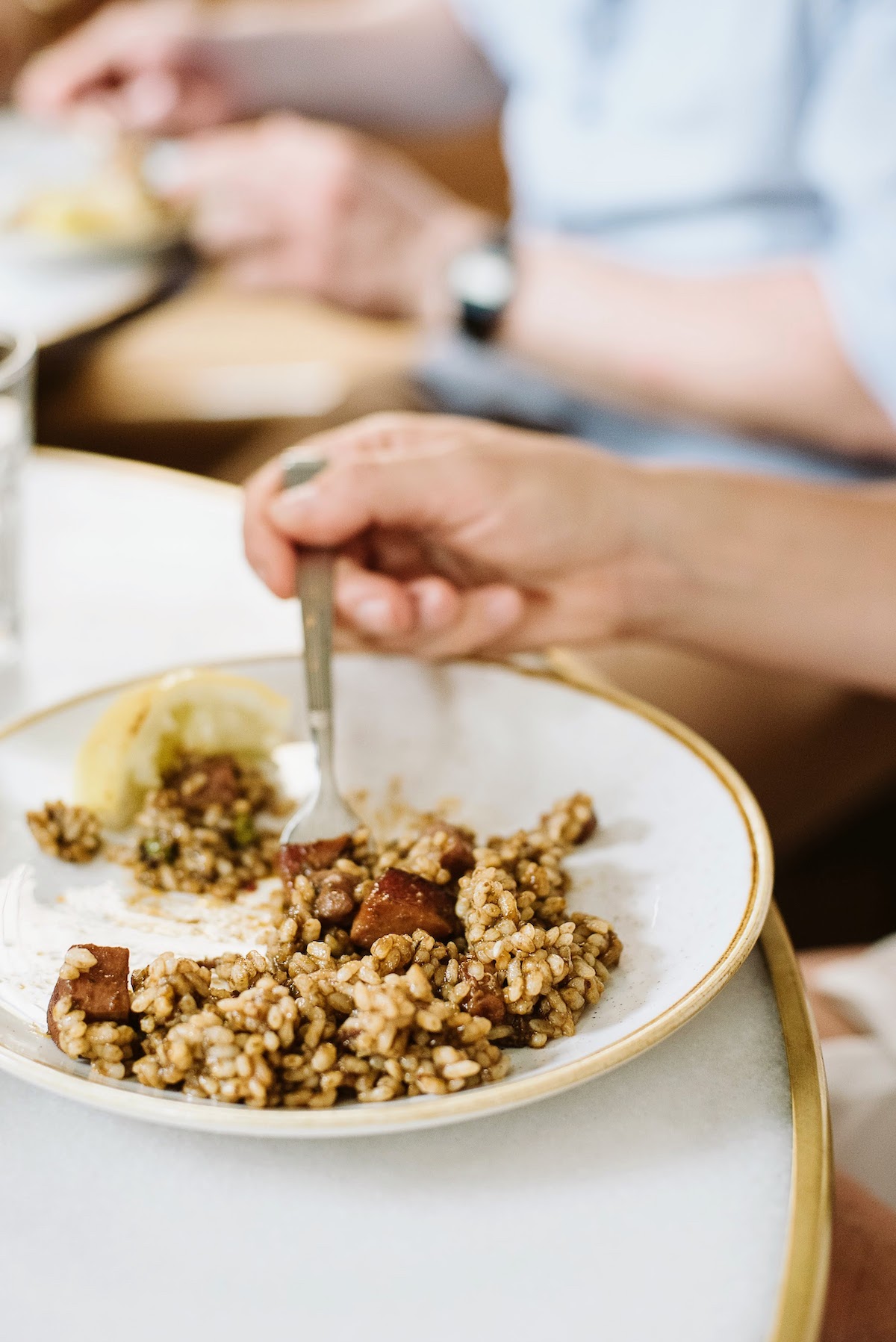 Person's hand eating a seafood and rice dish off of a white plate.