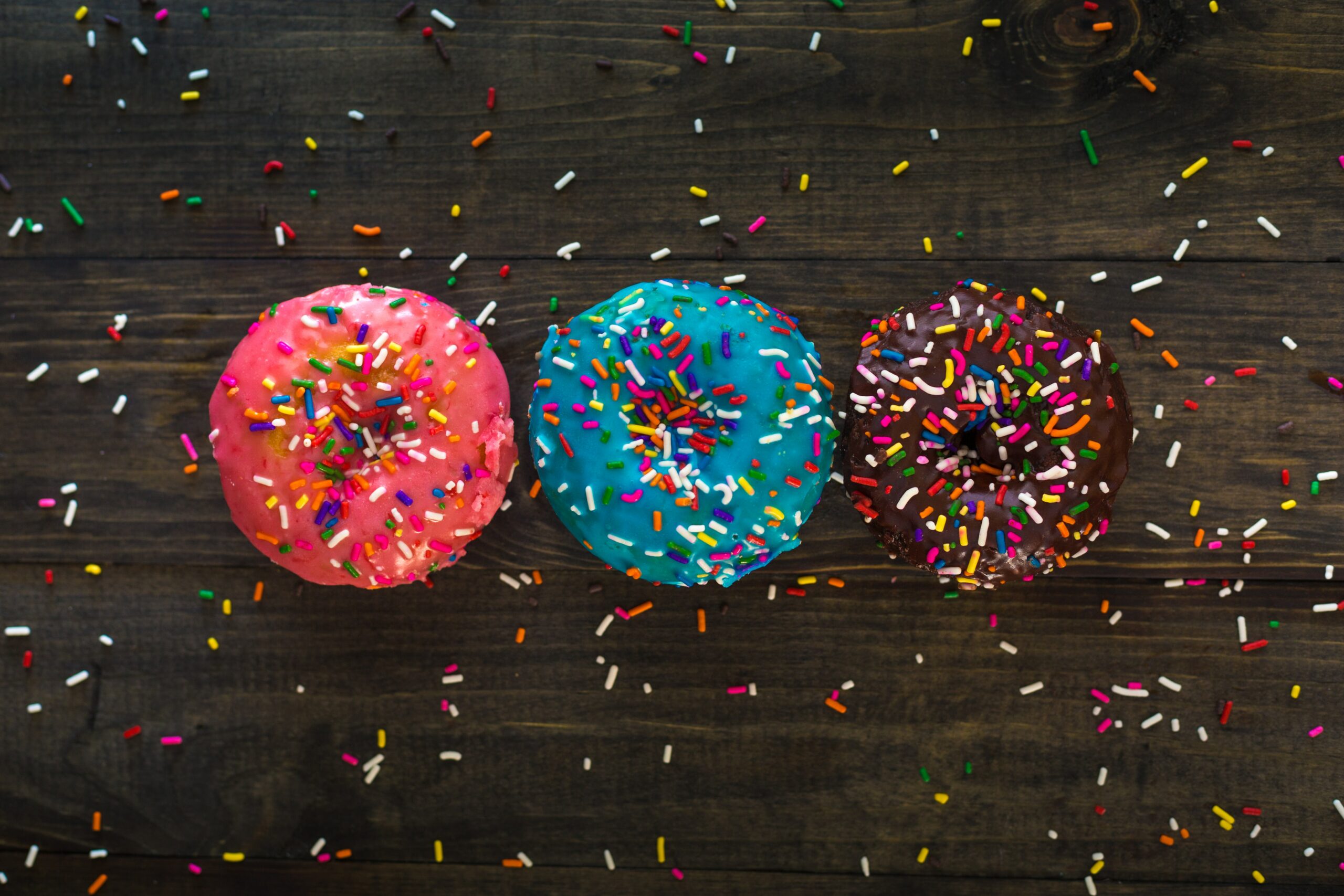 A pink, blue and chocolate donut are covered in sprinkles