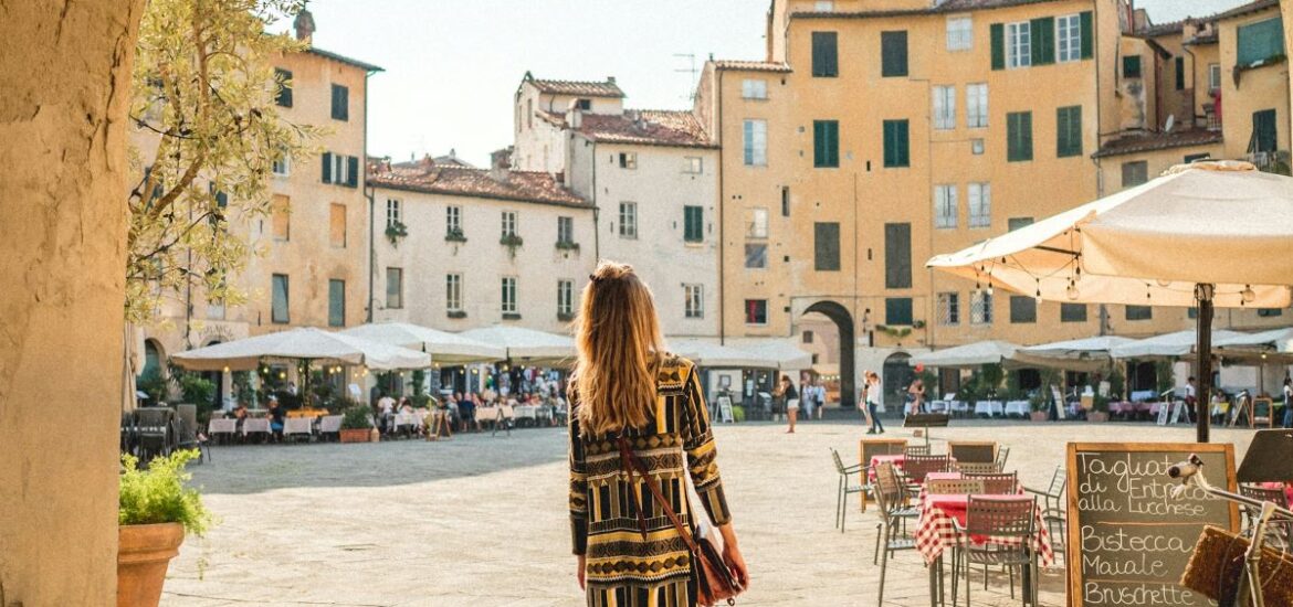 A woman walking towards a square in Lucca searching for the best restaurants in Lucca.