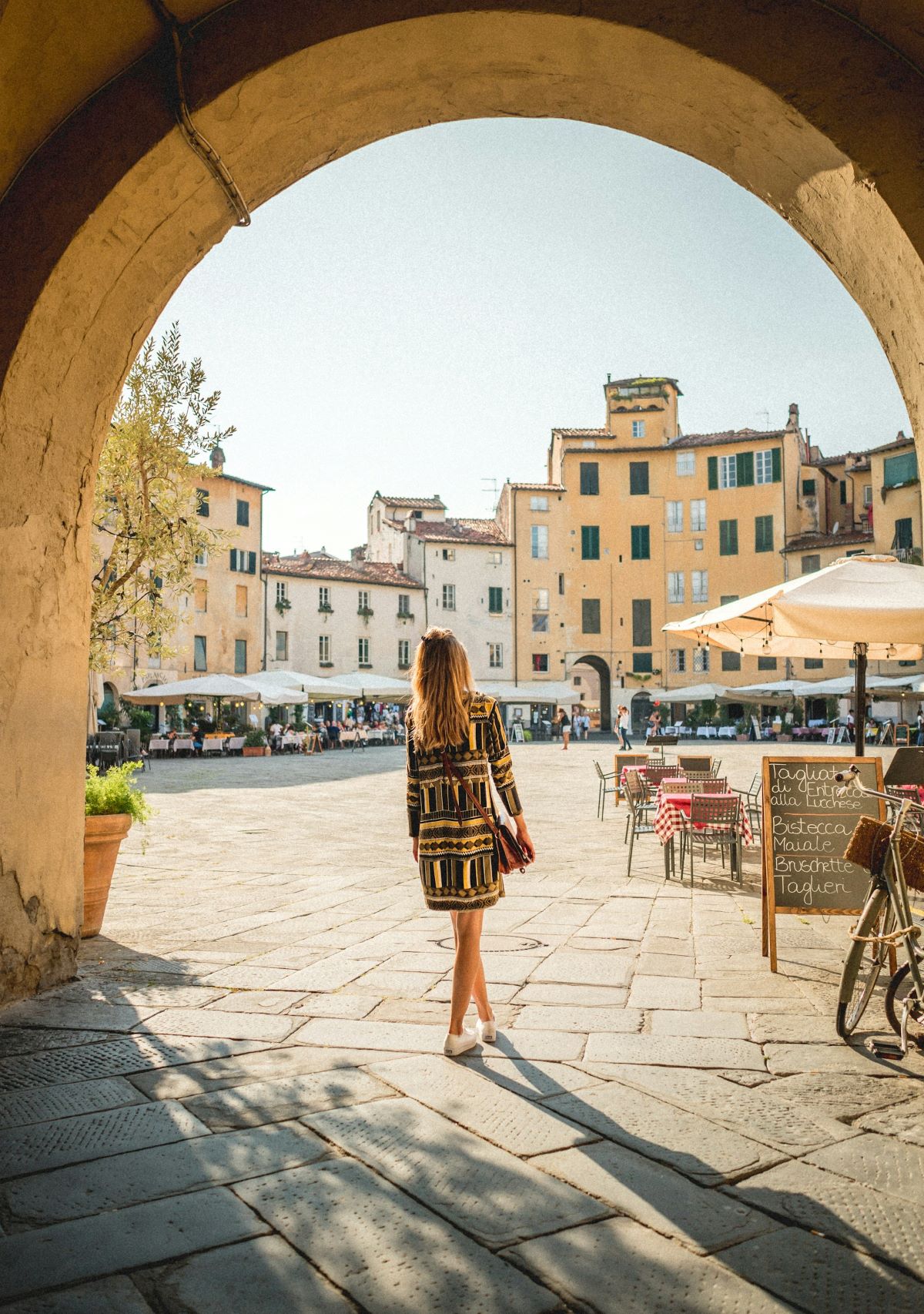 A woman walking towards a square in Lucca searching for the best restaurants in Lucca.