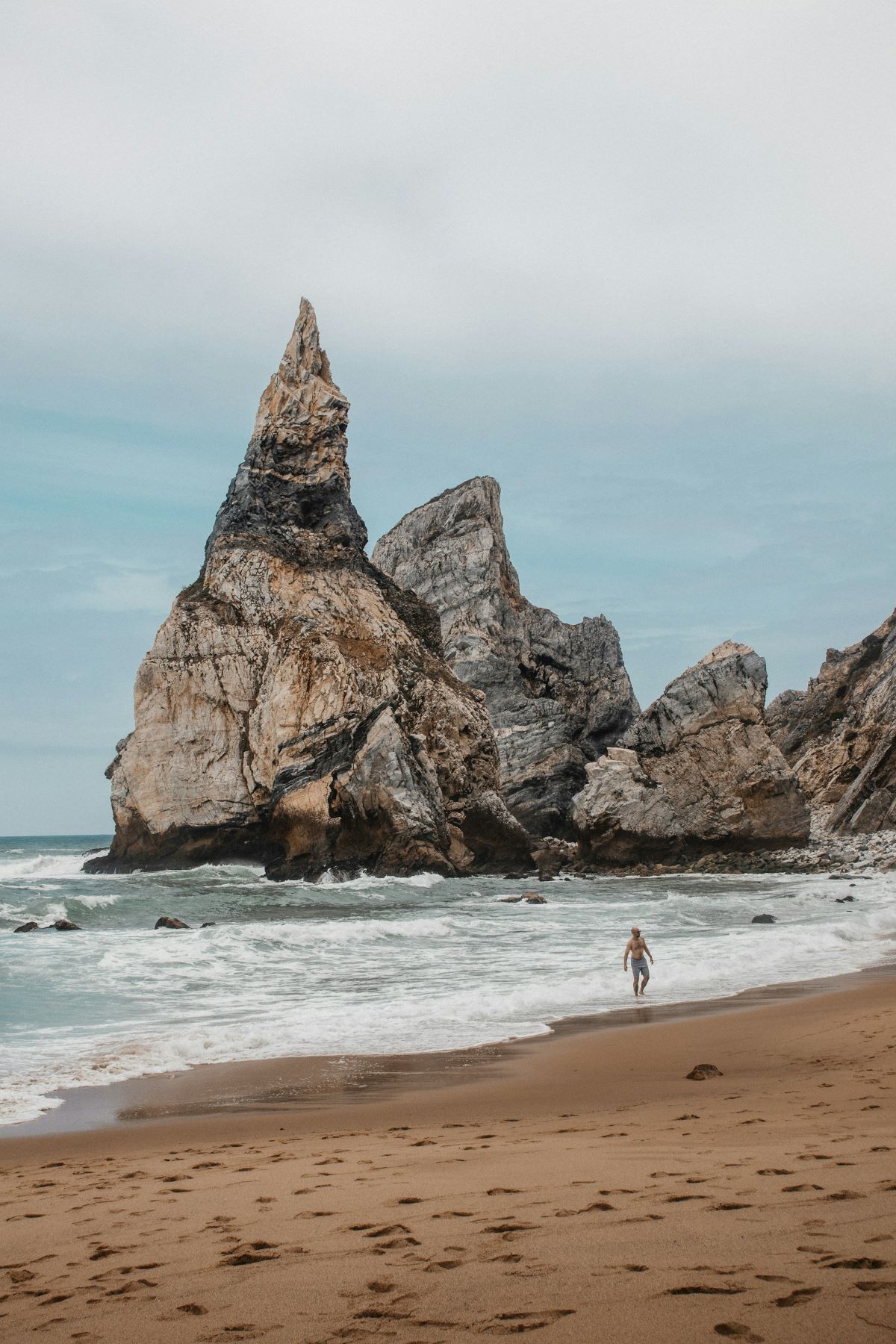 A man walking on the beach in Cabo da Roca as waves crash behind him. 