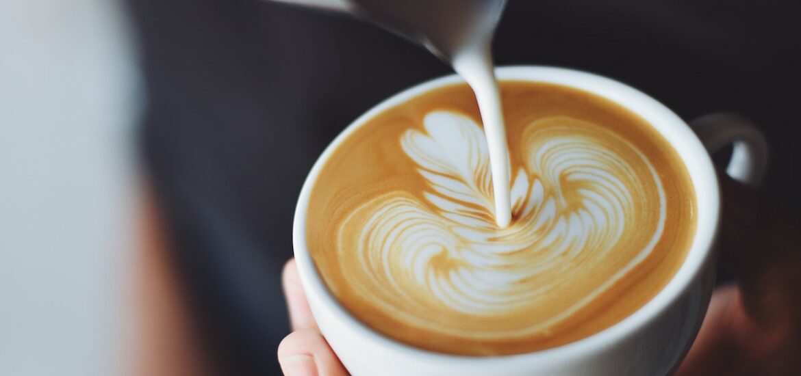 A person pours milk foam on coffee to make cappuccino art