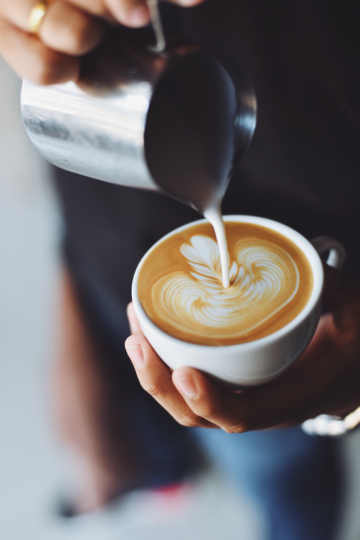 A person pours milk foam on coffee to make cappuccino art