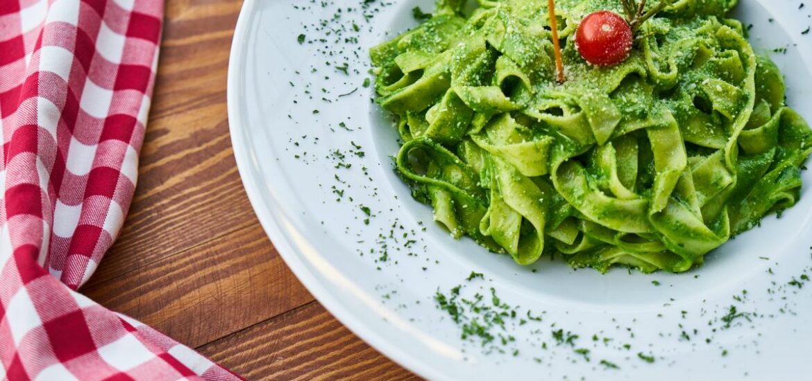 green pasta in white plate next to checkered towel