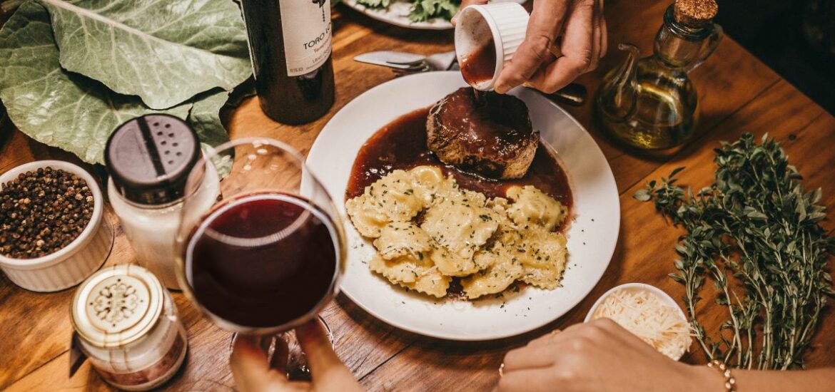 decorated table with pasta and meat dish and glass of red wine