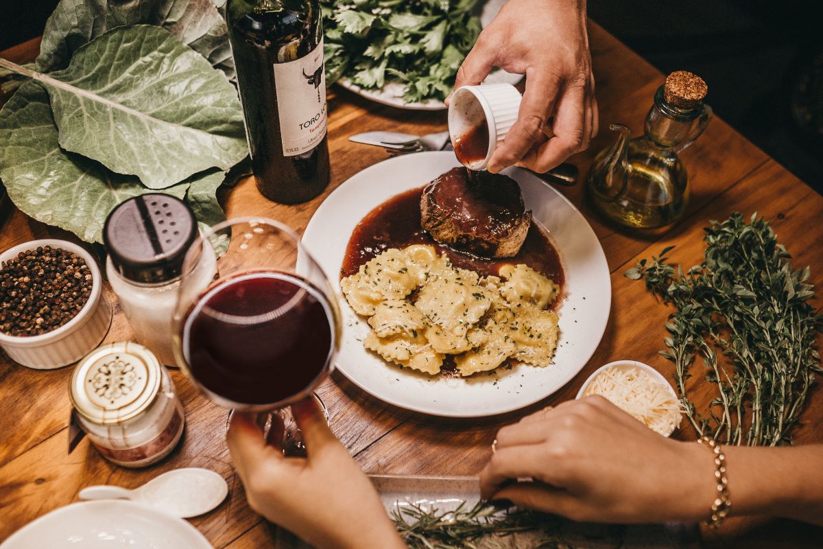 decorated table with pasta and meat dish and glass of red wine