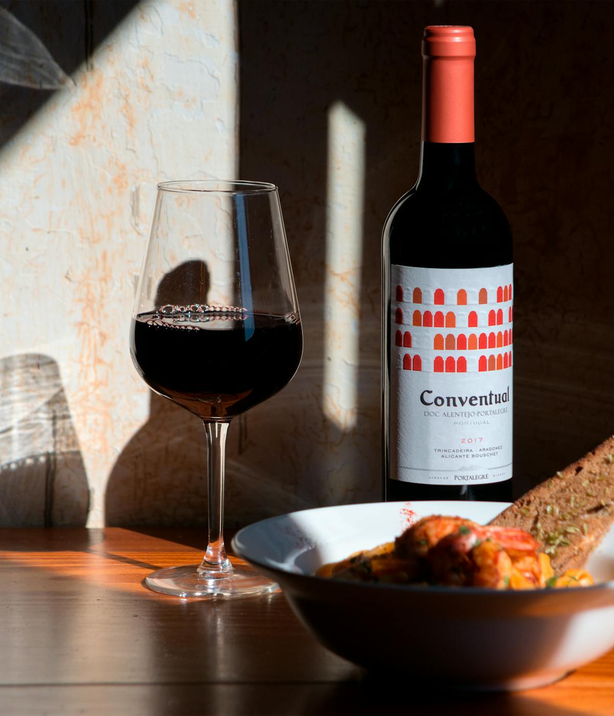 A bottle of red Portuguese wine next to a glass of wine and Portuguese food. 