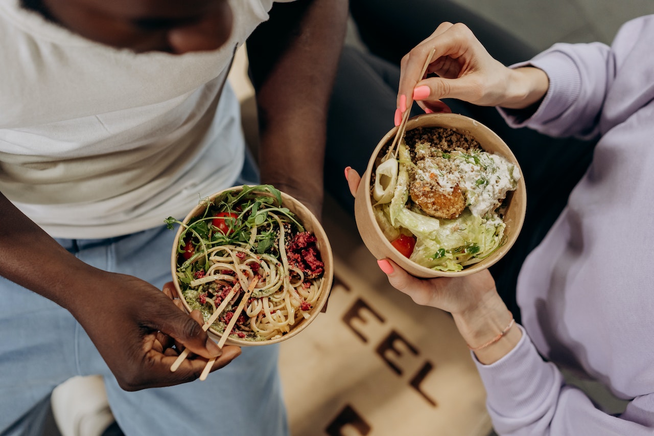 A couple eating food out of cardboard takeaway containers with chopsticks
