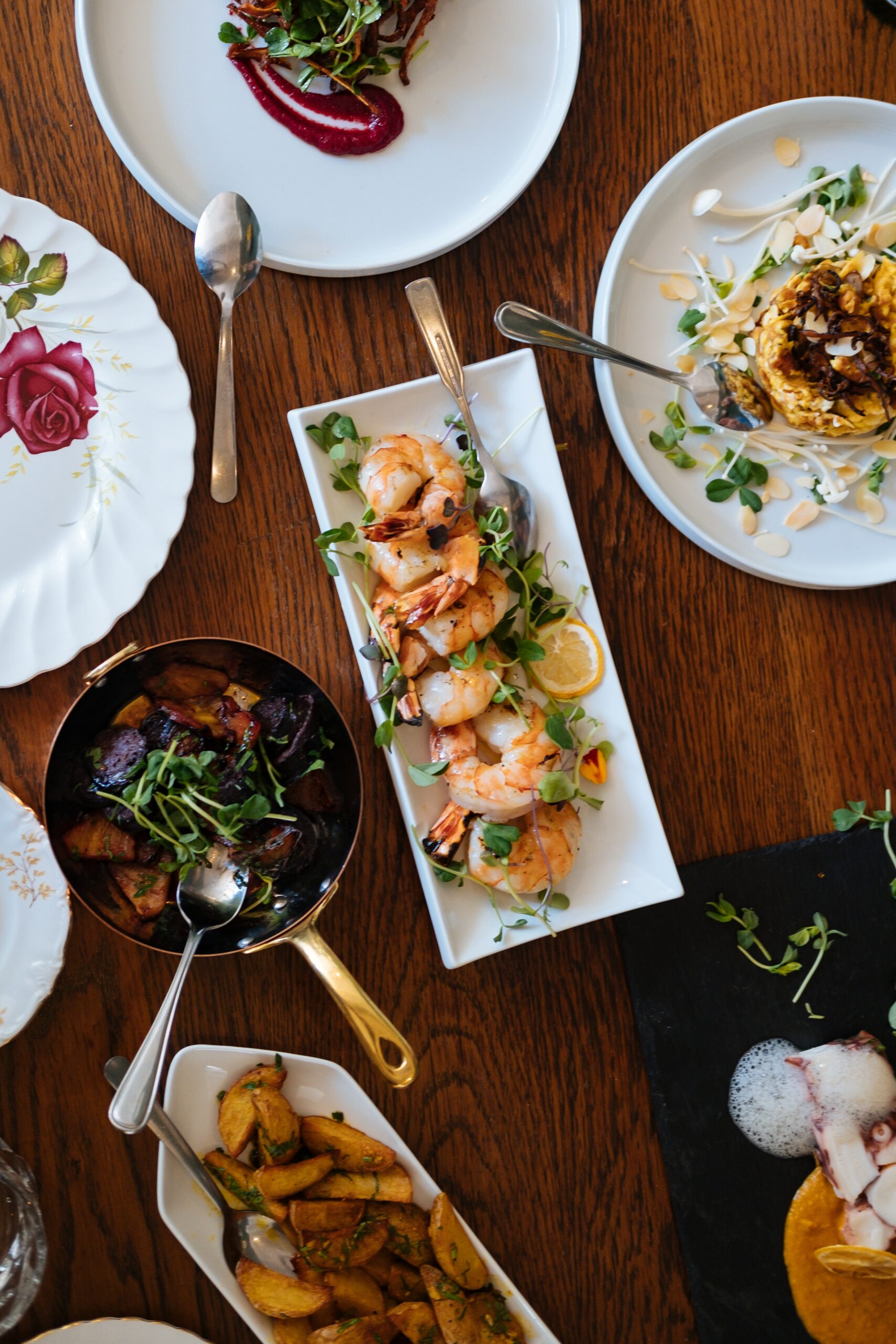 Small, shared plates of food on a table at a restaurant with shrimp, potatoes, foam, and more