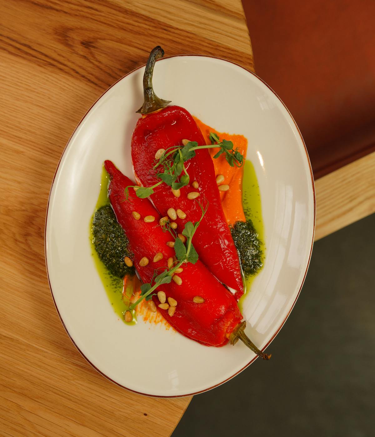 Two piquillo peppers on a plate with green sauce on top.