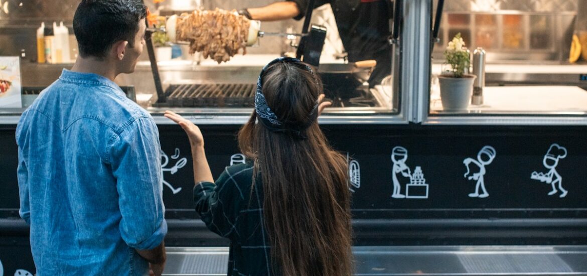 two people stand in front of the order window of a fodo truck