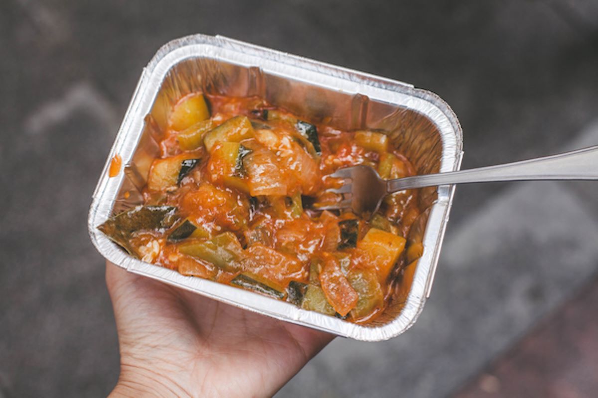 person holding container of vegetables in tomato sauce