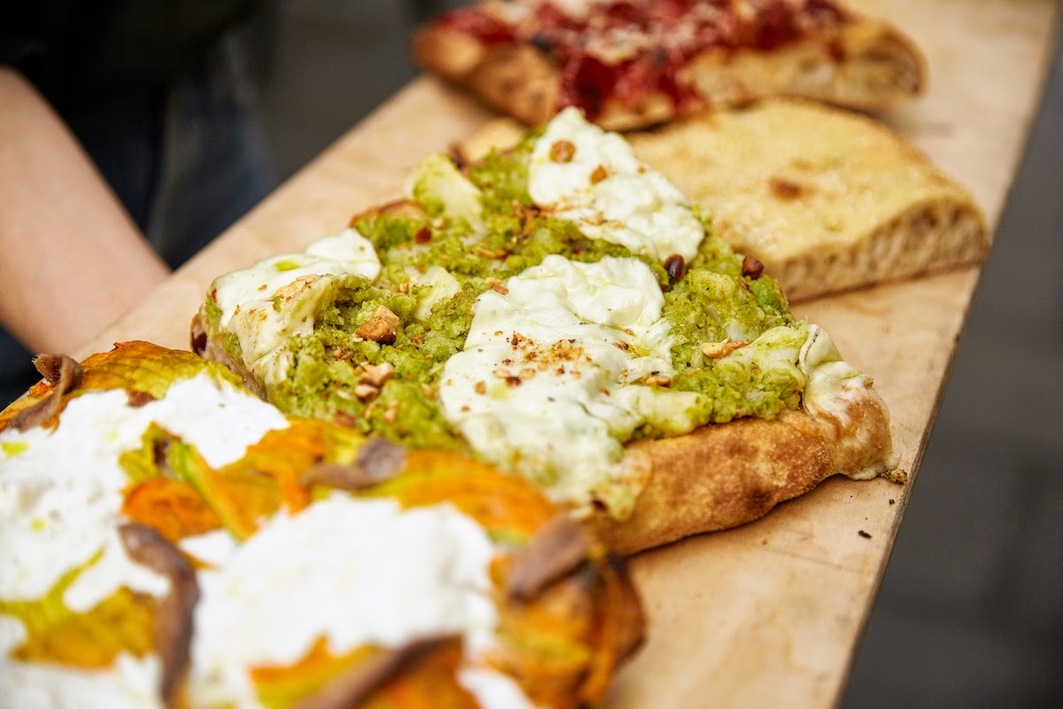 Wooden tray with several rectangular slices of pizza topped with gourmet ingredients.