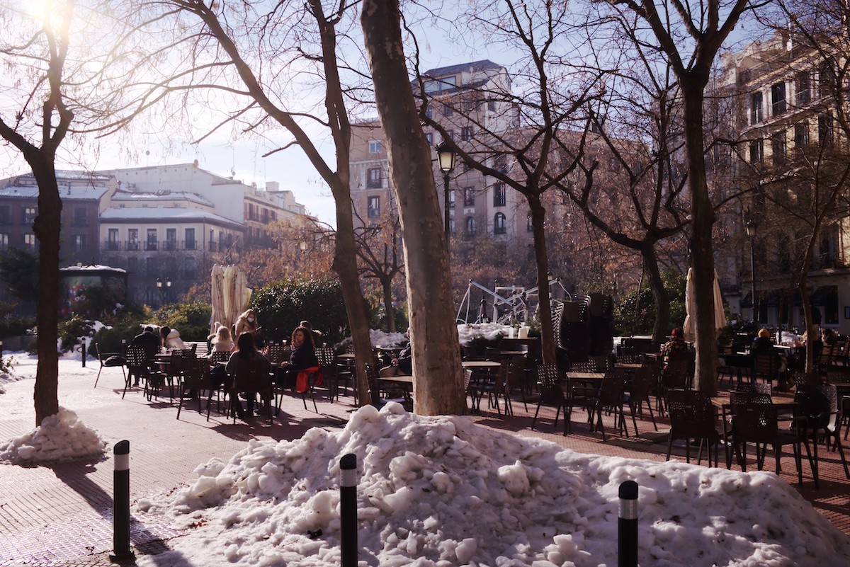 Sunny plaza with terrace seating and some piles of snow.