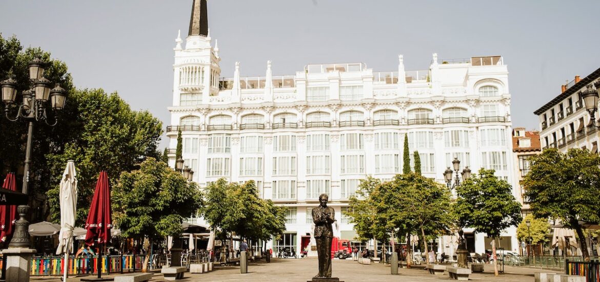 Urban plaza with a statue of a man in the foreground and a large white hotel in the background.