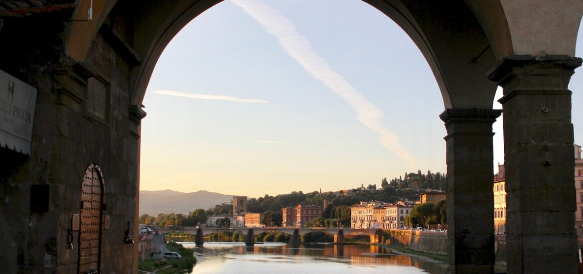 View of a city along the riverbank taken through an archway with a bridge visible in the background