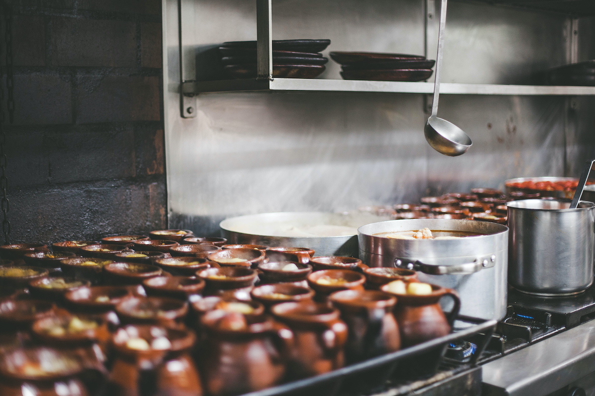 Clay jars and steel pots of stew simmering on a stove.