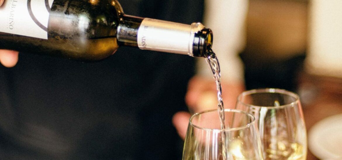 Bartender pouring two glasses of white wine on a wooden bartop.